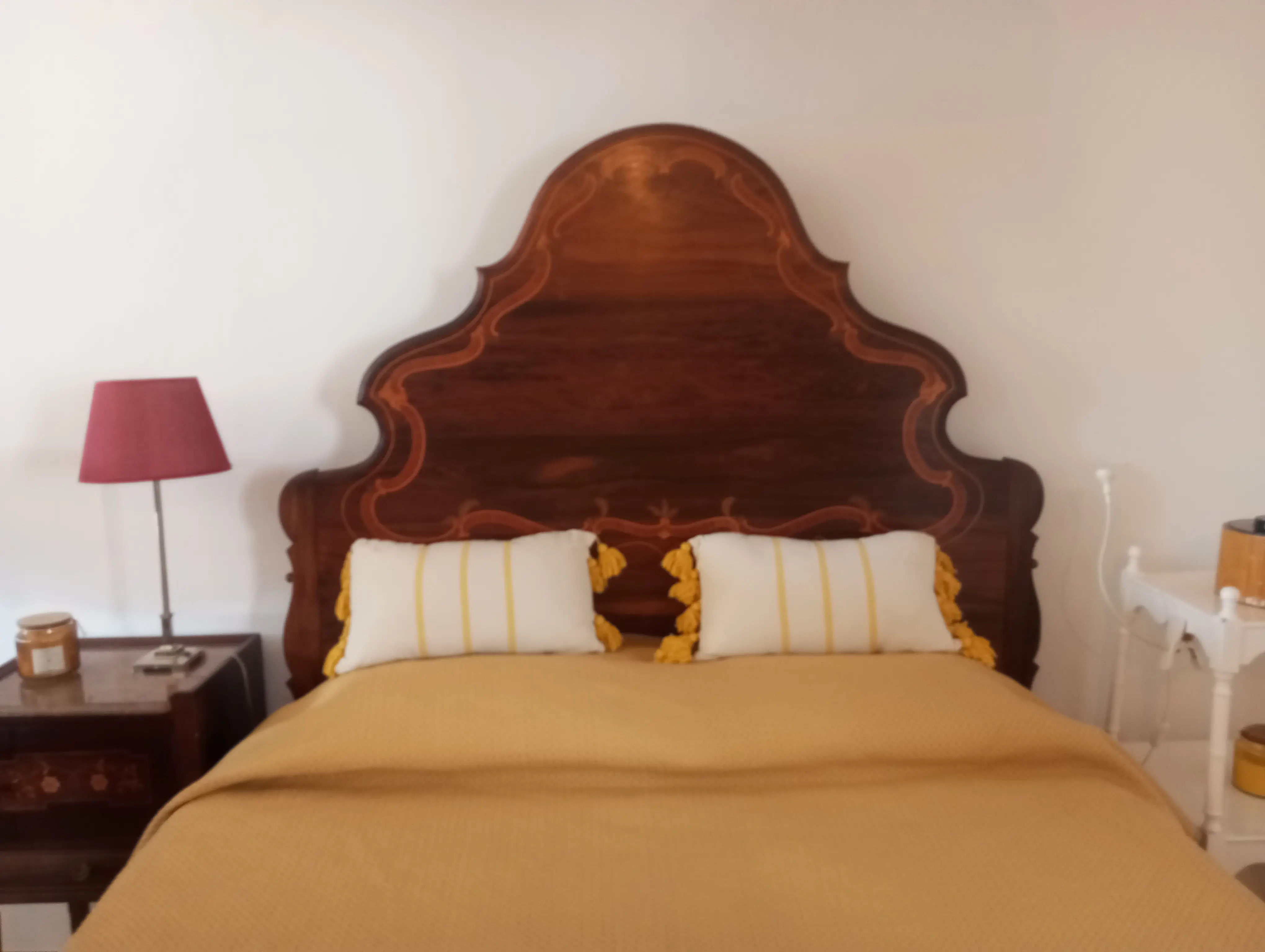 Cama de casal da Casa Pequena, com cabeceira de madeira entalhada e colcha amarela