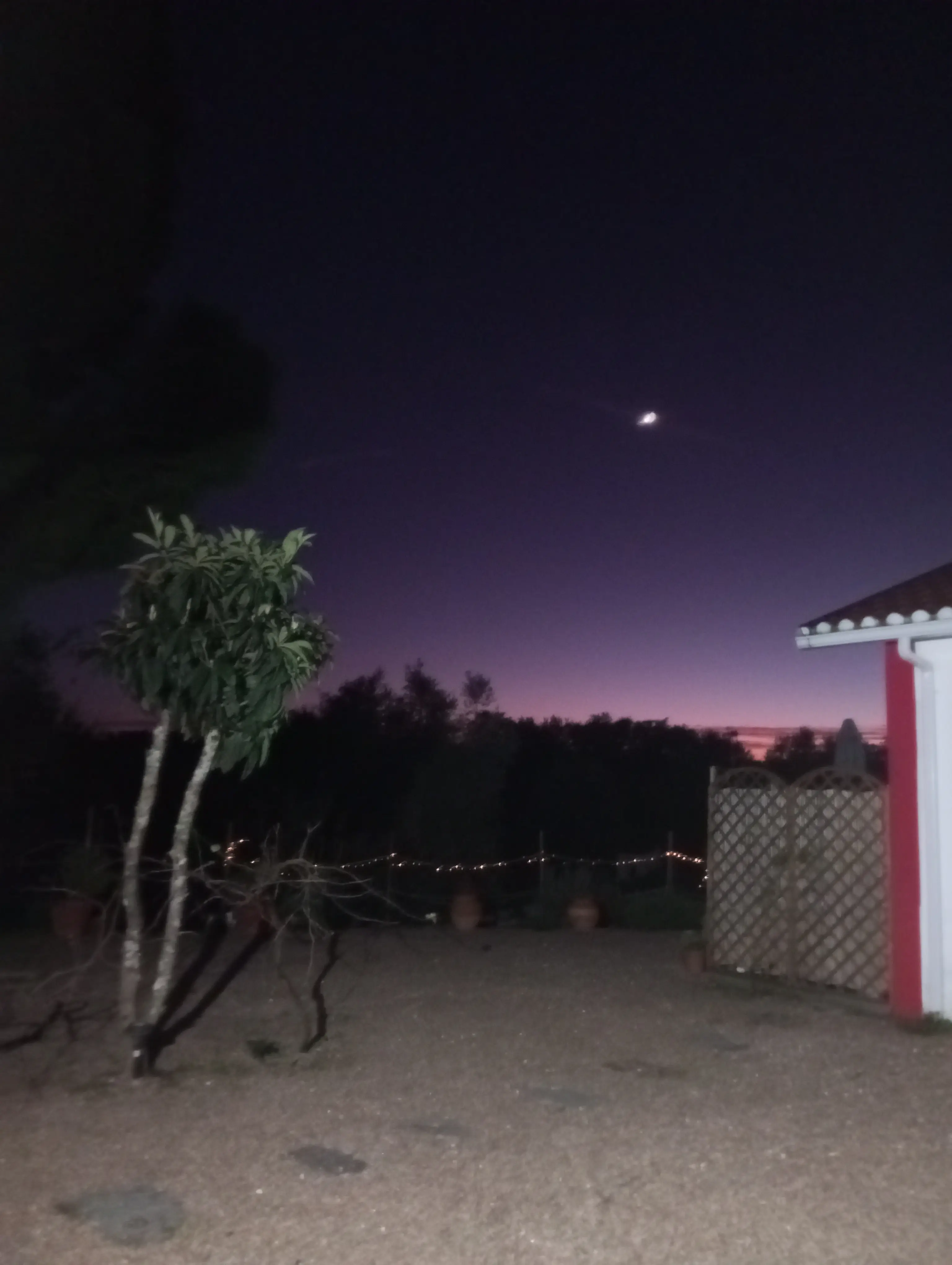 A propriedade ao anoitecer, com a lua sobre o horizonte roxo e as luzinhas acesas no jardim