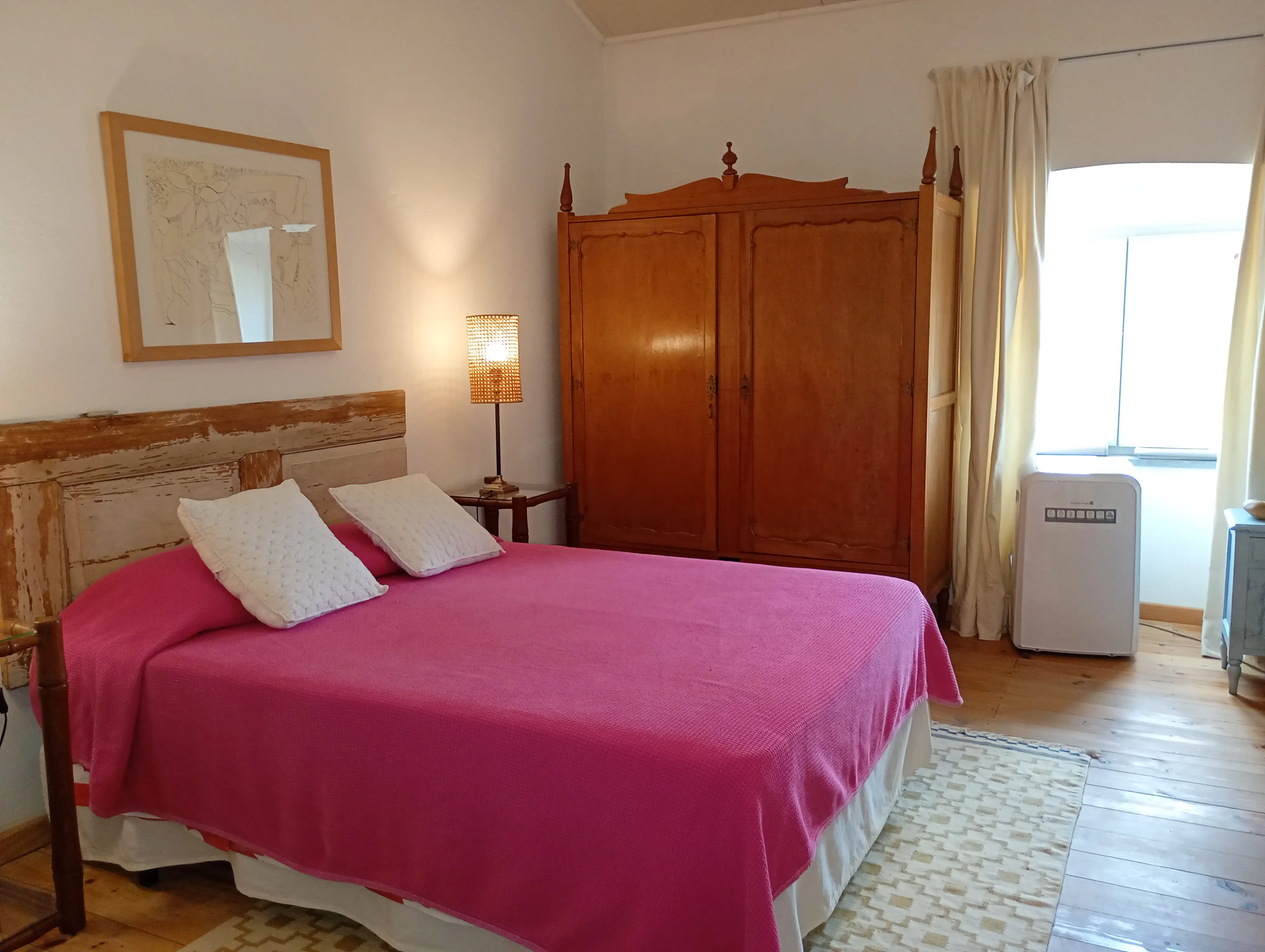 Quarto da Casa Principal com cama de casal, colcha rosa, roupeiro antigo de madeira e chão de tábua